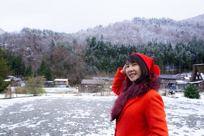 Smiling young woman standing in snow against trees during winter