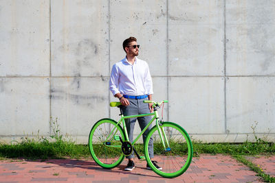 Young bearded man with sunglasses standing with bike outdoors