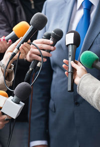 Cropped hands of journalists holding microphones in front of businessman