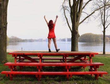 Rear view of woman with umbrella on bench at lake