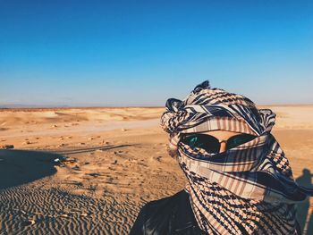 Portrait of woman face covered with scarf in desert against clear sky