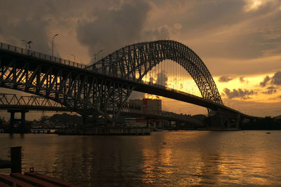 Illuminated bridge over river at sunset