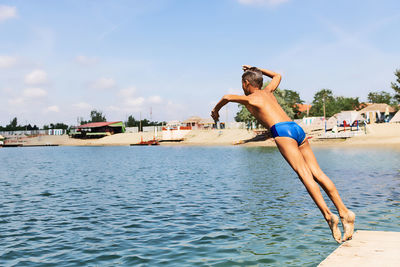 Full length of shirtless man jumping in sea against sky