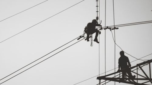 Low angle view of men working on cable against sky