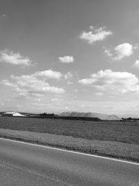 Road by agricultural field against sky