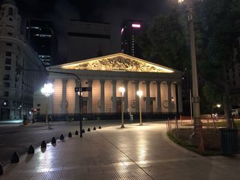 People walking on illuminated street amidst buildings at night