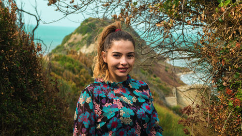 Portrait of smiling young woman standing against mountain