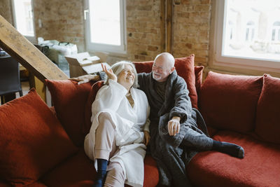 Happy senior couple spending leisure time while sitting on sofa at home