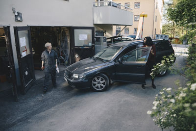 Female mechanic looking at customer opening car door outside auto repair shop