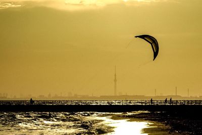 Silhouette person flying over sea against sky during sunset