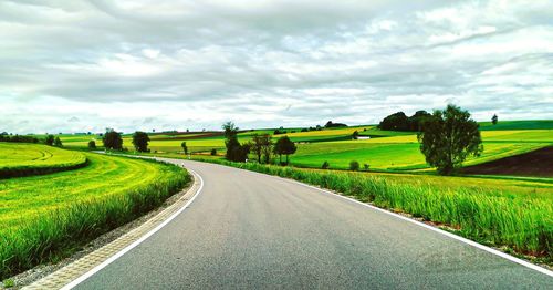 Empty road amidst field against sky
