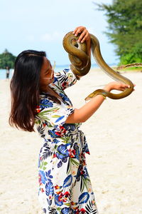 Young woman holding snake while standing at beach