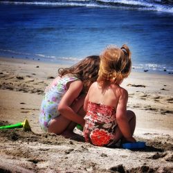 Friends sitting at beach during sunny day