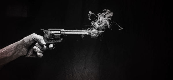 Cropped hand holding gun against black background