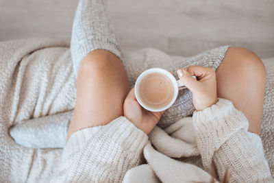 Overhead photo of a woman in a cozy sweater and warm socks. woman holding a cup of coffee.