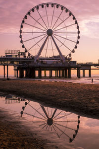 Silhouette ferris wheel by sea against sky at sunset