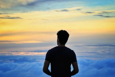 Rear view of man standing against cloudy sky during sunset