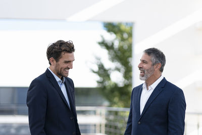 Businessmen laughing while standing at office building terrace