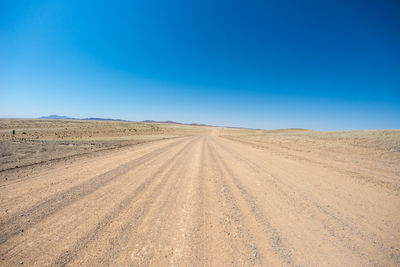 Tire tracks on desert against clear blue sky