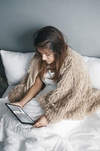 High angle view of woman using digital tablet while sitting on bed