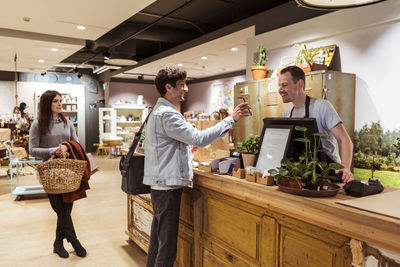 Male customer with woman showing mobile phone to cashier while paying at checkout counter