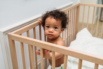 High angle portrait of cute shirtless baby boy standing in crib at home