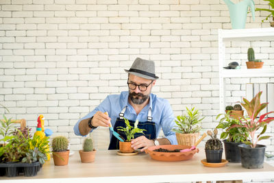 Young man with potted plants on table against wall
