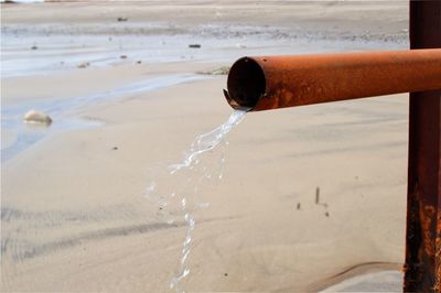 Close-up of water falling from pipe on beach