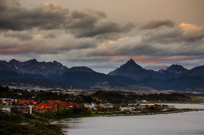 Scenic view of residential buildings by mountains against sky during sunset