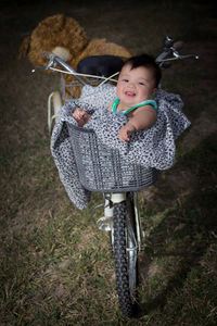 Portrait of cute baby boy sitting in bicycle basket on field