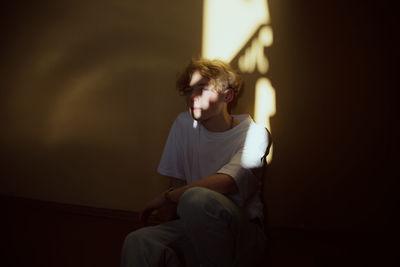 Young man looking away while sitting on wall at home