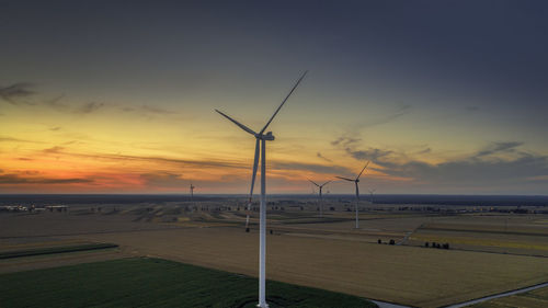 Wind turbines on field against sky during sunset