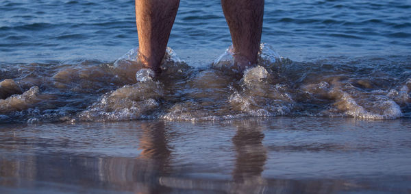 Low section of man standing in sea