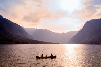 Silhouette people on lake against sky during sunset