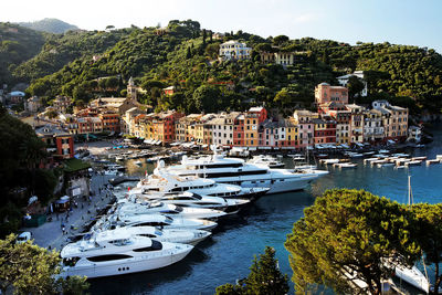 Yachts moored in sea at harbor by village against blue sky