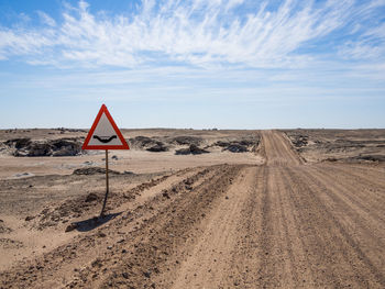 Road sign in desert against sky