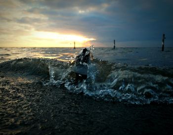 Sea waves splashing on rock at shore during sunset