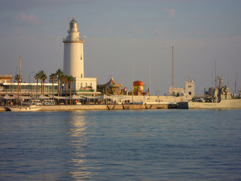 Lighthouse by sea against buildings in city