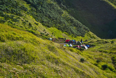 People by tent on field against mountain