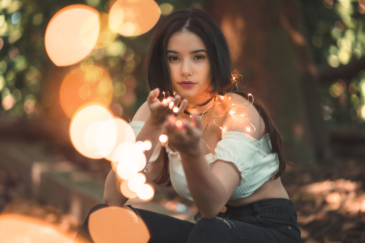 night, looking at camera, illuminated, one person, young adult, portrait, focus on foreground, leisure activity, young women, beautiful woman, holding, weapon, standing, real people, outdoors, lifestyles, tree, people