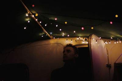 Man looking away while standing at entrance of illuminated motor home