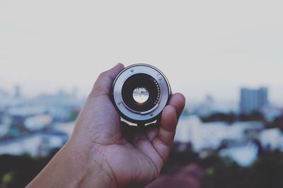 Close-up of hand holding lens against sky