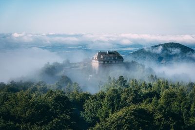 House surrounded by trees against sky during foggy weather