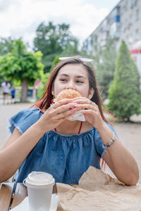 Portrait of young woman eating burger at street cafe