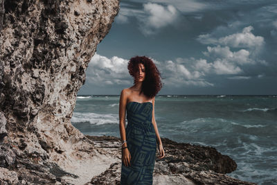 Woman standing on rock by sea against sky