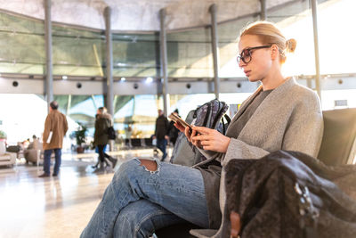 Mid adult woman using smart phone while sitting at airport