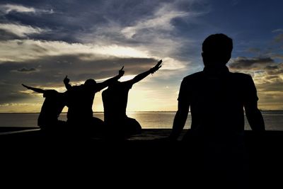Silhouette people on beach against sky during sunset