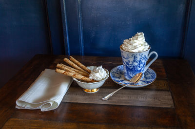 Gourmet hot chocolate and whip cream in a nautical china mug with cookies on a rustic table 
