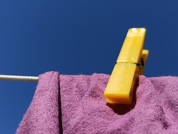 Low angle view of yellow clothespins on blue against sky