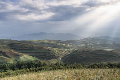 Scenic view of landscape against cloudy sky and sunbeam